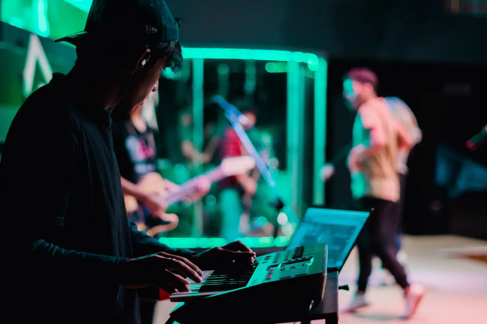 Concert live baigné de lumière verte, un musicien au clavier de synthétiseur au premier plan et le groupe derrière.