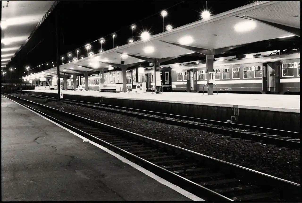 Quai de gare désert la nuit, éclairé par les lampadaires, avec une voiture de train à l'arrêt.