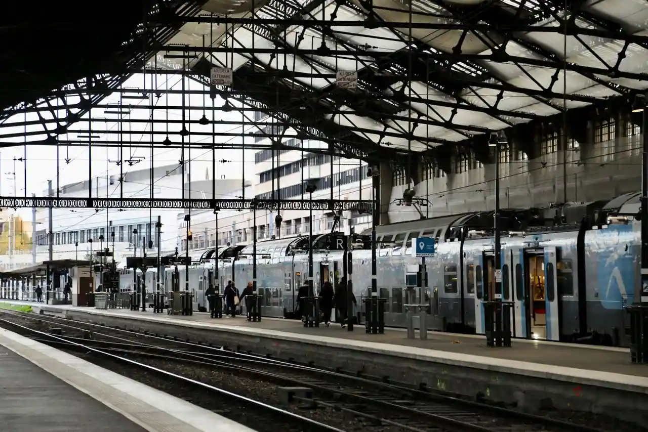 Train et voyageurs le long d'un quai couvert sous la verrière d'une gare ferroviaire parisienne.