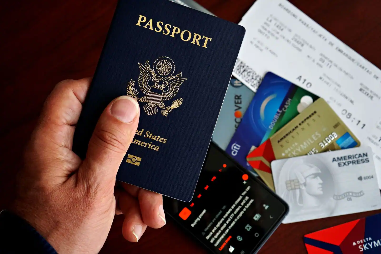 Main tenant un passeport devant une carte d'embarquement et des cartes bancaires, prêt à voyager.