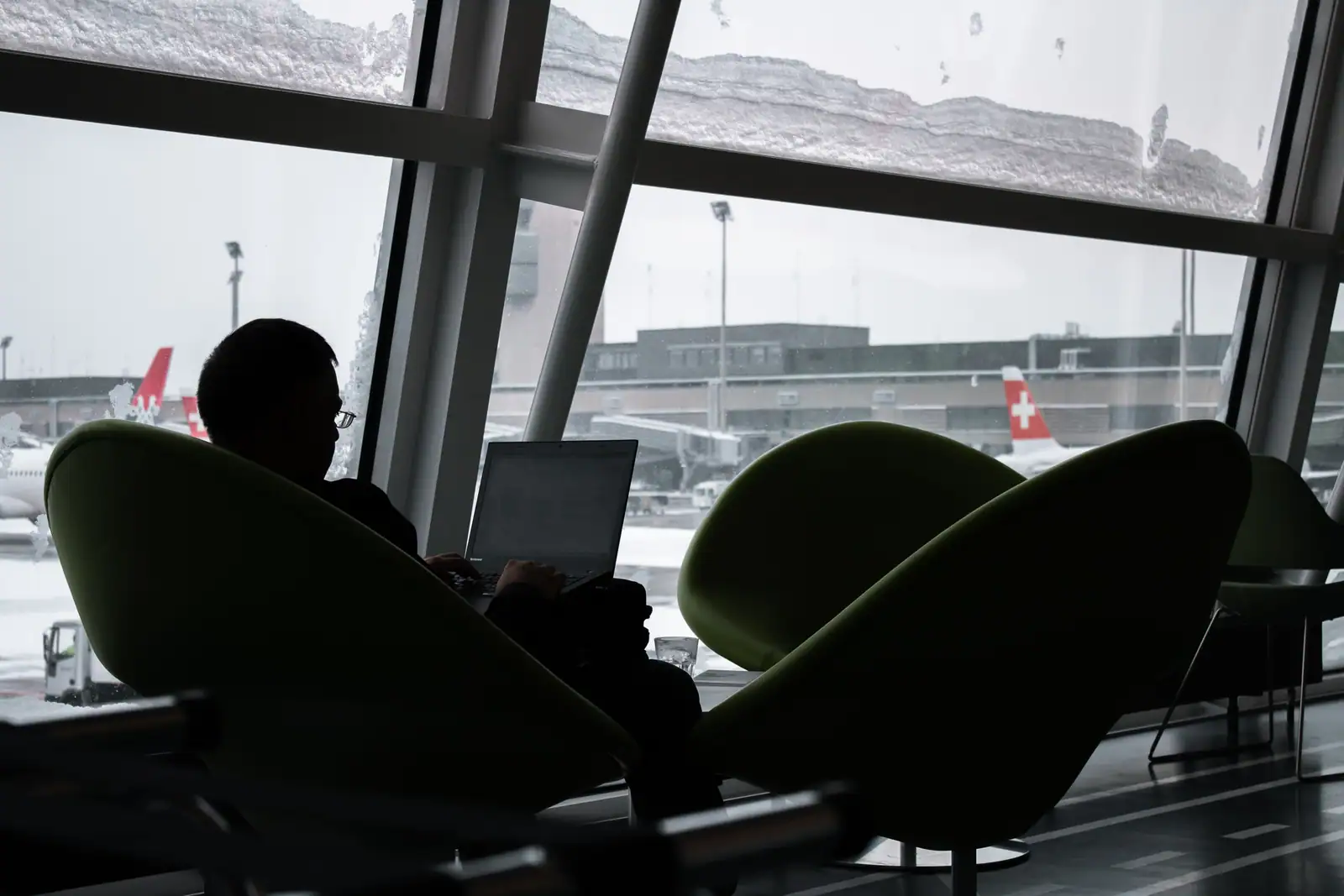 Voyageur installé dans un salon d'aéroport devant un ordinateur portable, avions visibles dehors.