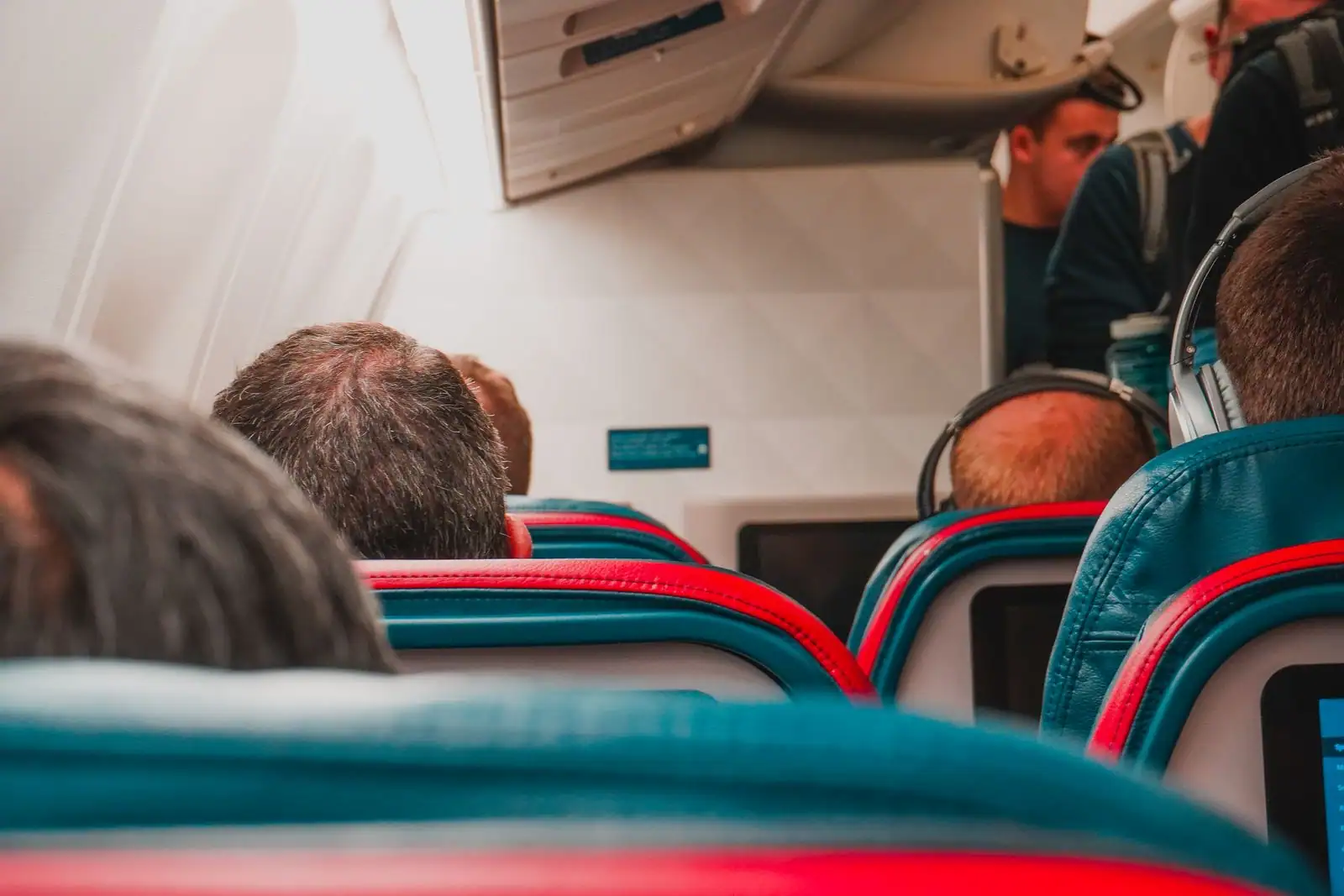 Intérieur d'une cabine d'avion de ligne, passagers assis vus de dos entre les sièges colorés