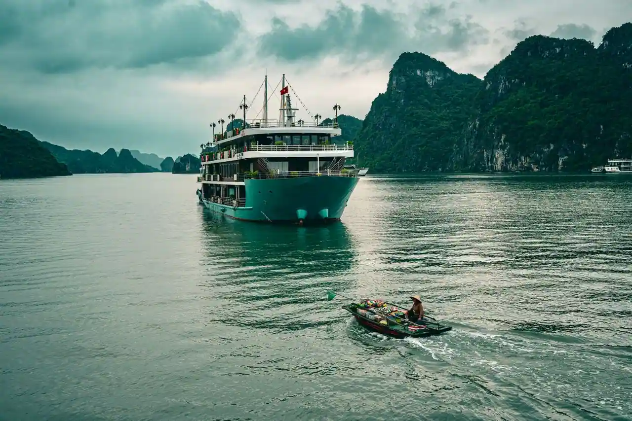 Un bateau de croisière et une petite embarcation locale devant les reliefs karstiques d'une baie du Vietnam.