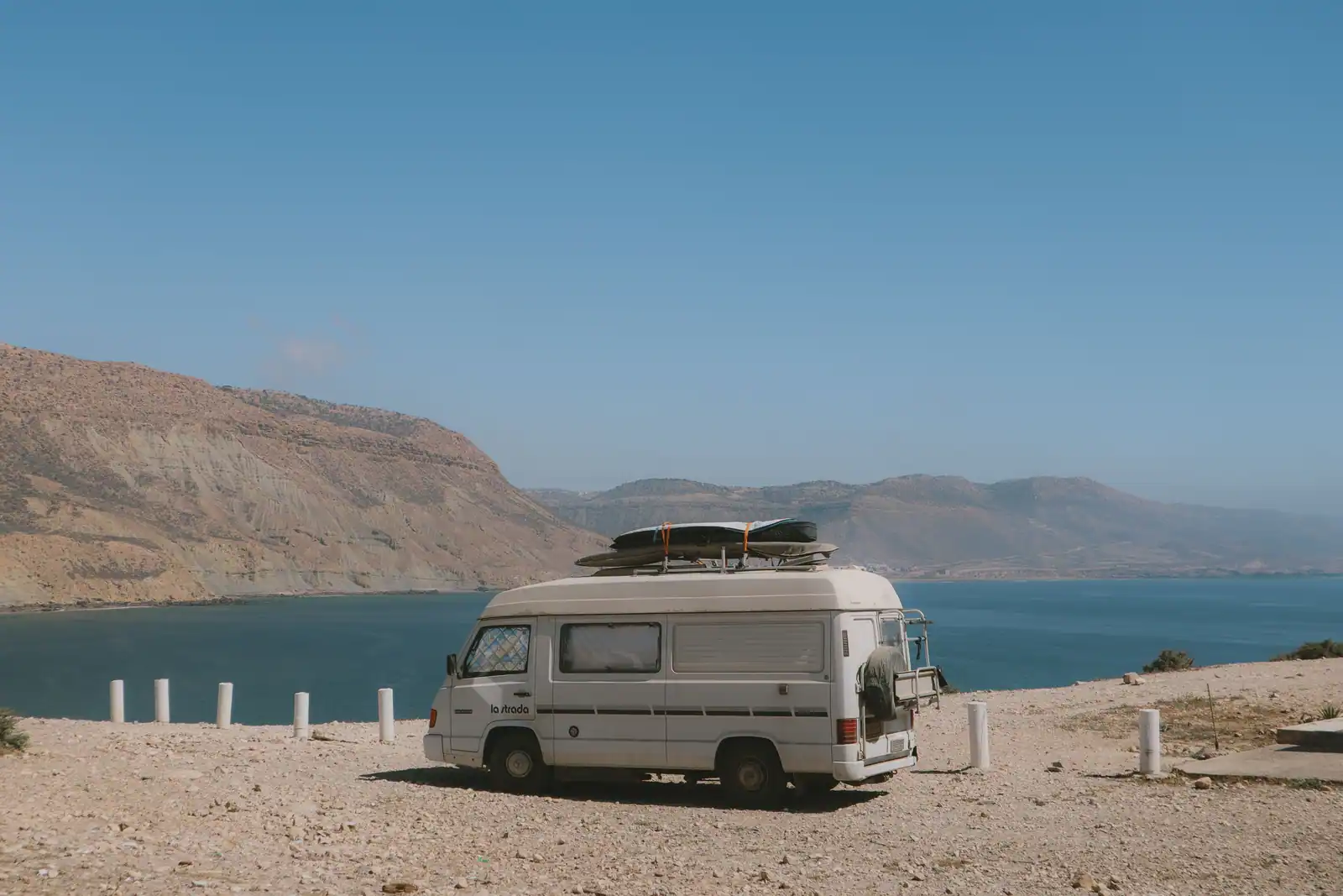 Camping-car aménagé stationné sur un rivage aride face à un plan d'eau, entouré de collines au Maroc